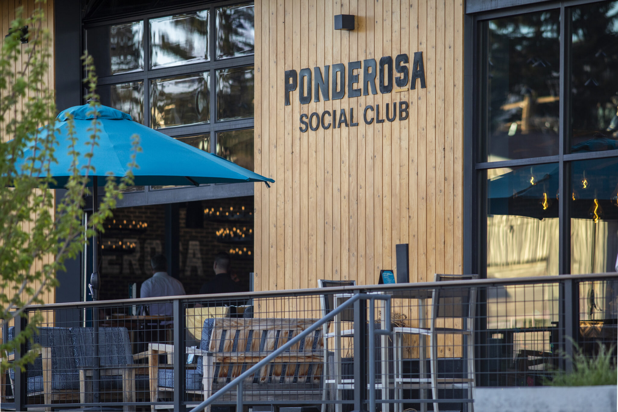 Ponderosa Social Club cedar storefront with a blue umbrella and outdoor seating in Bozeman
